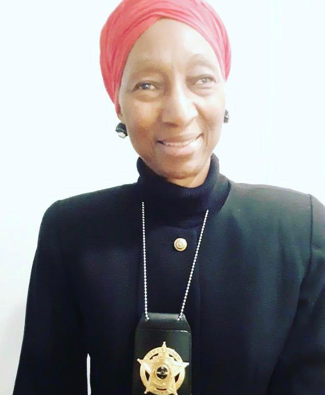 Person in dark clothing wearing a sheriff badge on a chain.